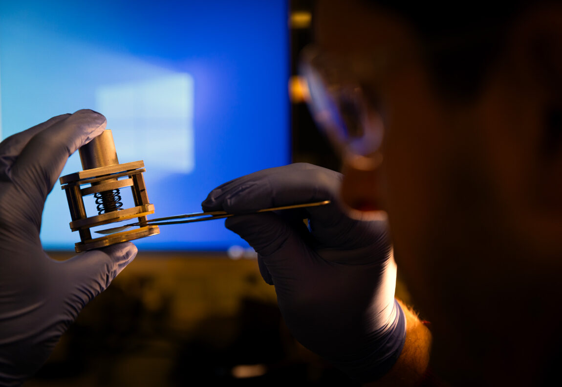 A photo of a man holding large tweezers and a small object