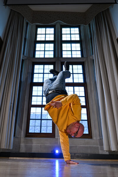 A photo of a man breakdancing; he is shown upside down balancing on one hand