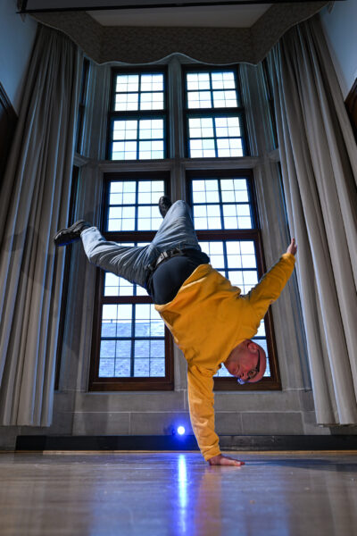 A photo of a man breakdancing; he is shown upside down balancing on one hand
