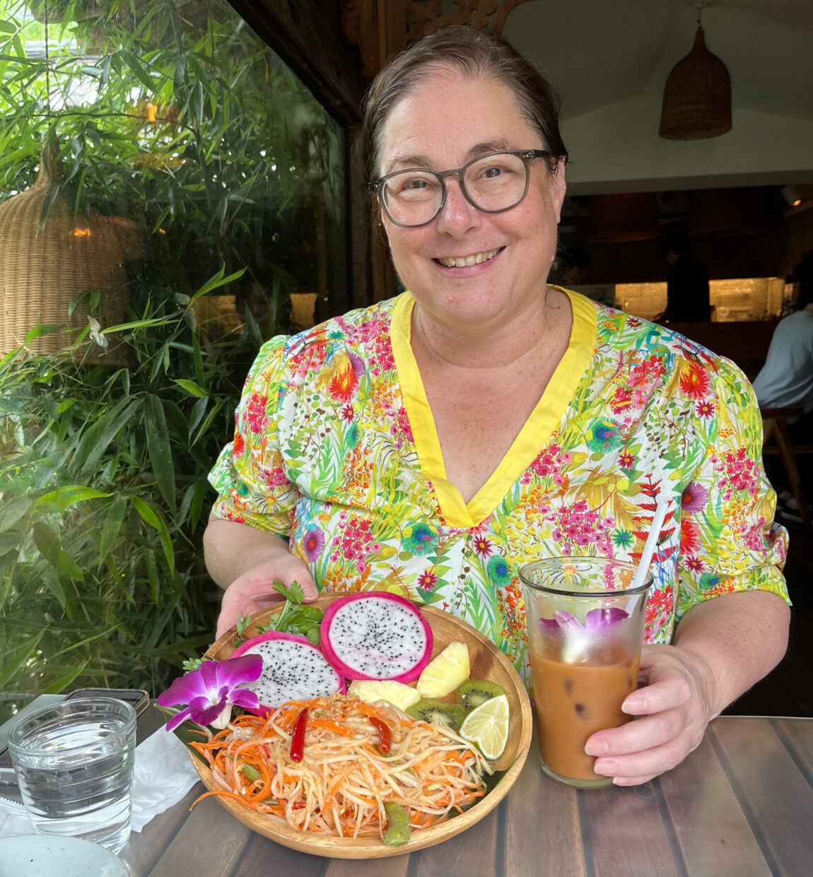 A photo of a woman sitting at a table showing a plate of food and holding an iced coffee drink