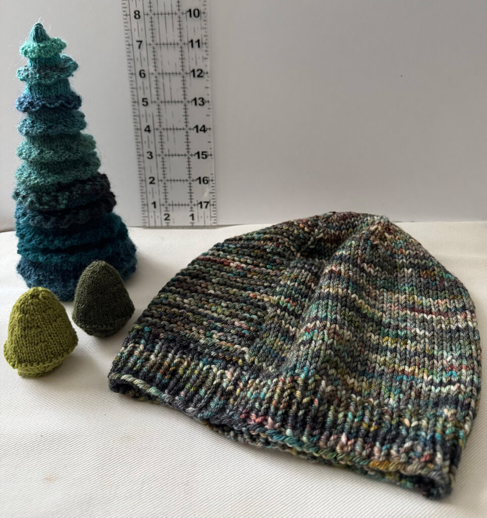 A photo of a fir tree, tiny confiers and a hat, all knitted by Sandra Wiley