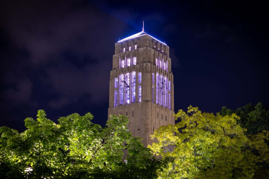 The lights atop Burton Tower shed a faint purple hue onto the clouds in the dark night sky. Image credit: VP Communications, Regents of the University of Michigan