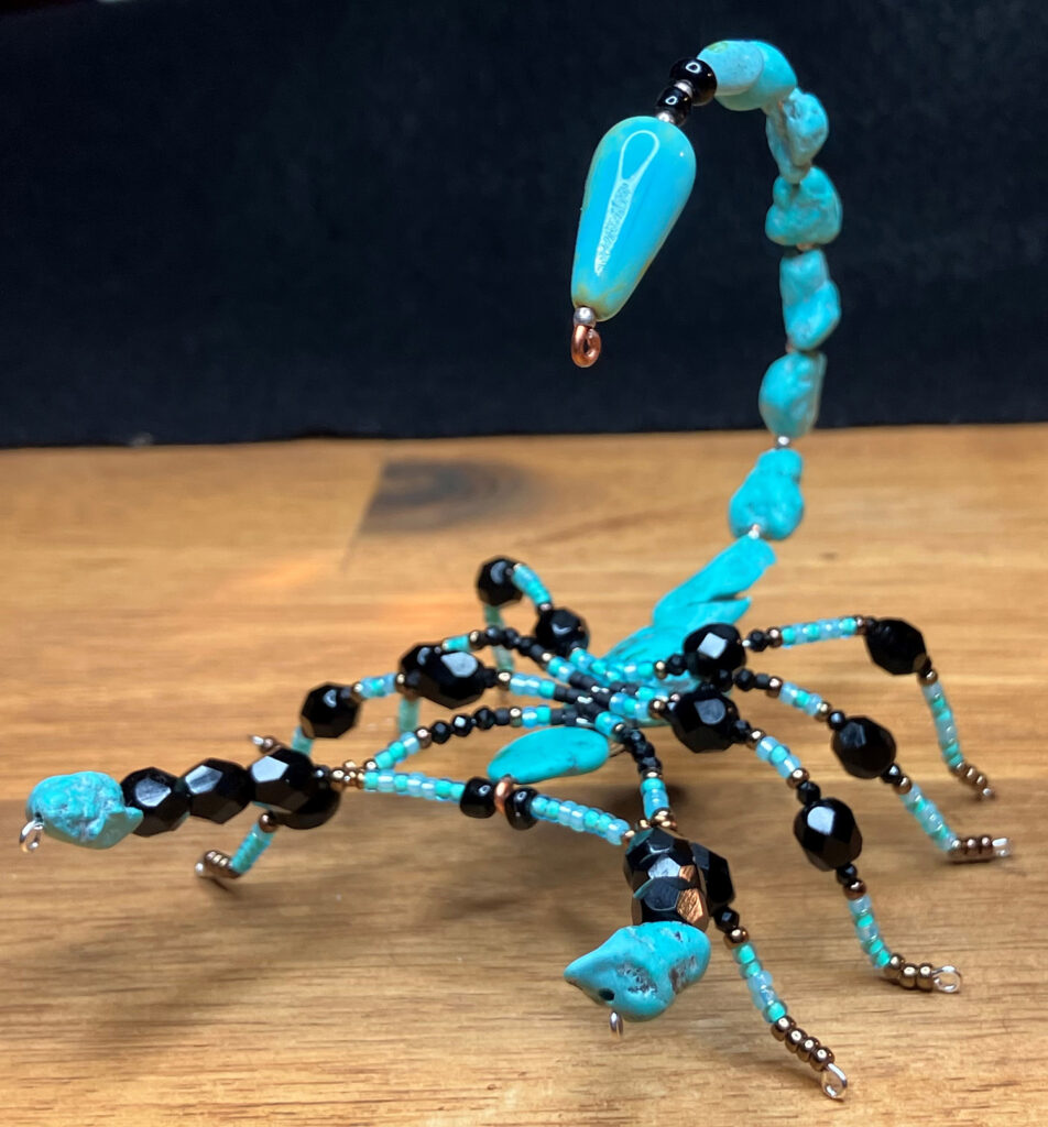A photo of a blue beaded critter that looks like a scorpion but is jewelry