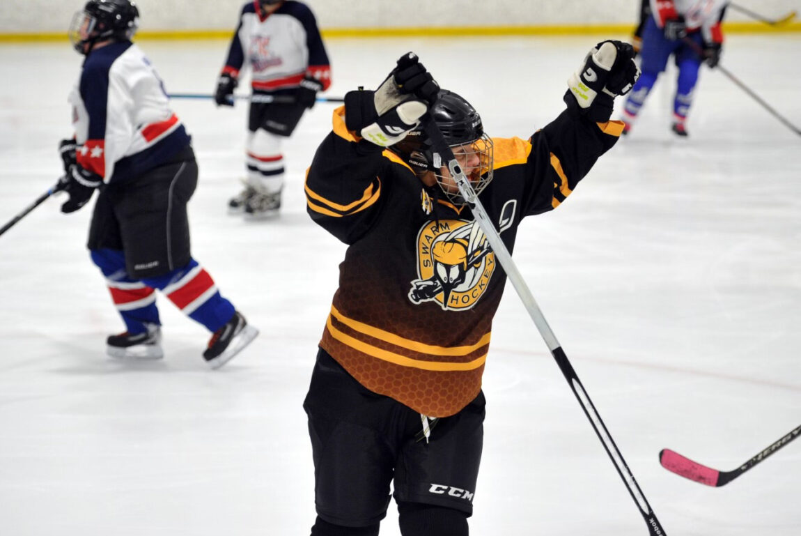 A photo of a woman celebrating after scoring a goal with other hockey players in the background