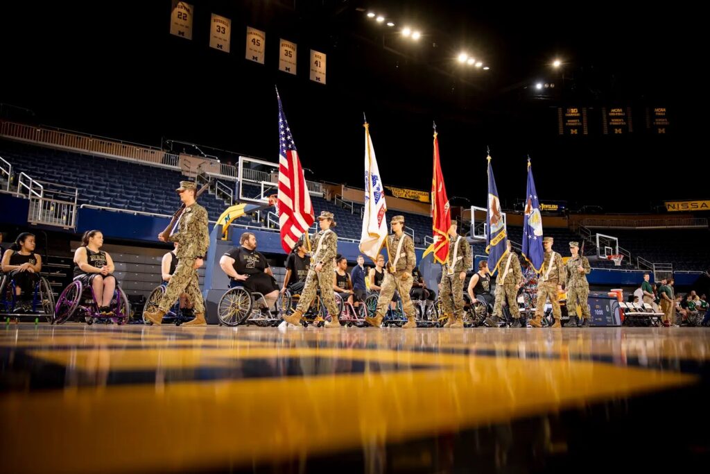 A photo of men and women in military uniform carrying flags before a basketball game