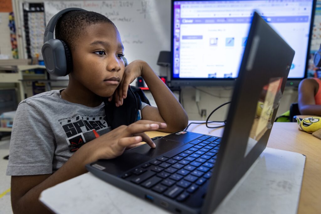 A student wearing headphones concentrates on the digital coursework displayed on the screen of their laptop.