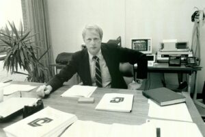 Black & white photo of young caucasian man named James Duderstadt. He is seated at his desk in the College of Engineering at the University of Michigan.