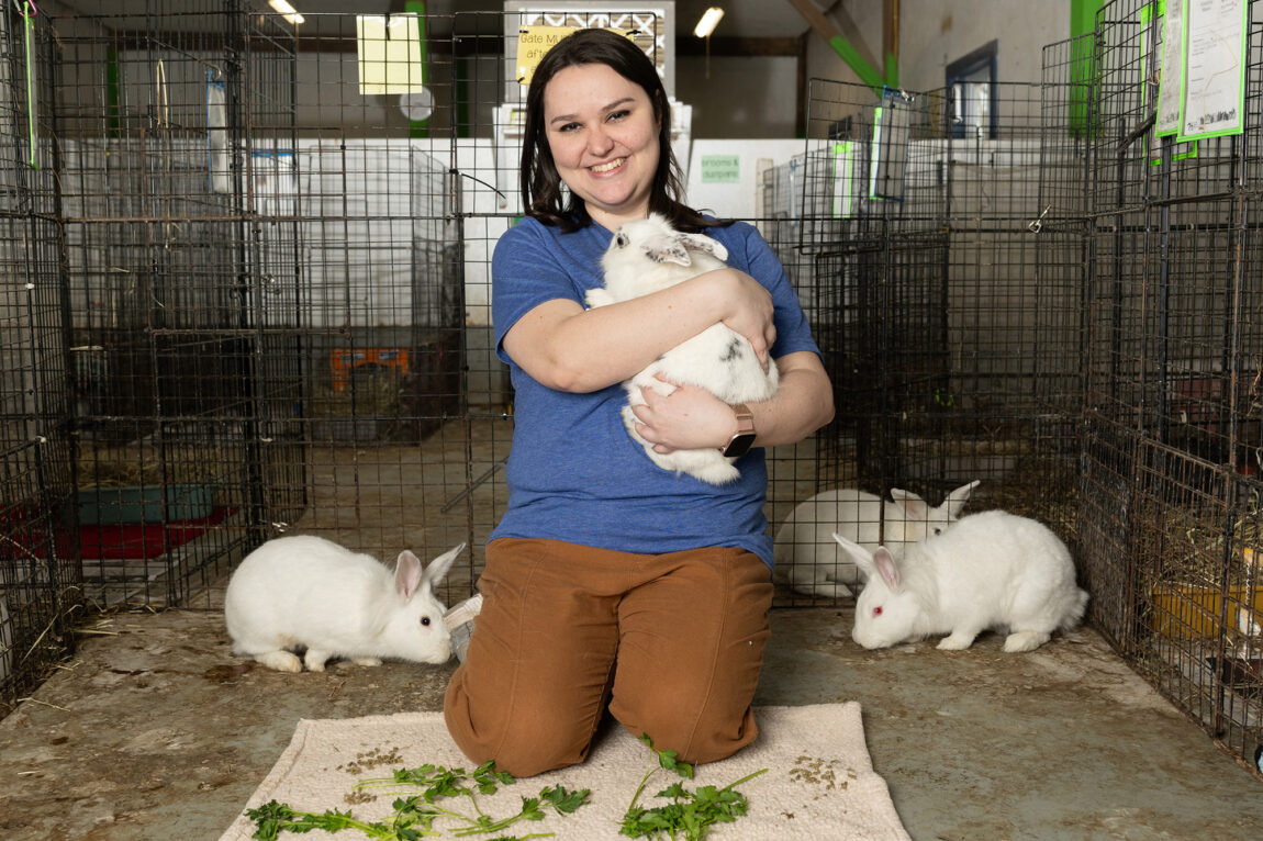 A photo of a woman kneeling while holding a rabbit with three other rabbits on the ground near her