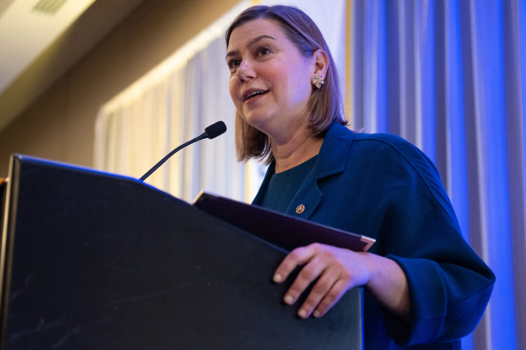 A photo of a woman standing and speaking at a lecturn