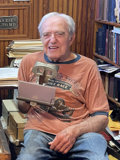 A photo of a man sitting in a chair holding a stereoscopic viewer