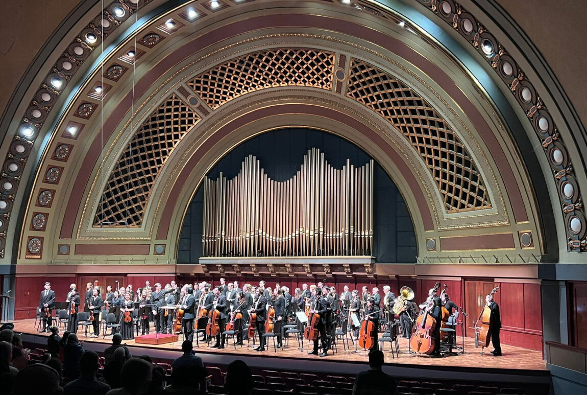 A photo of an orchestra standing after a performance in a music hall