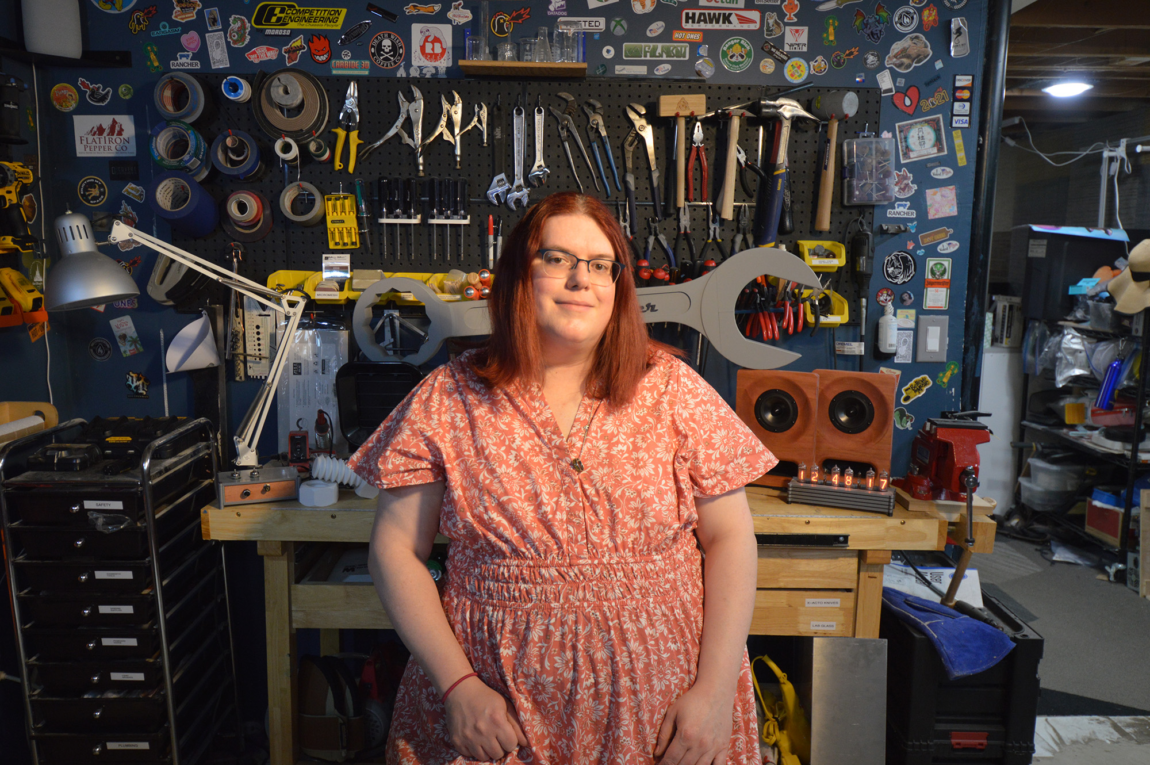 A photo of a woman at a work bench with many tools and projects in the background
