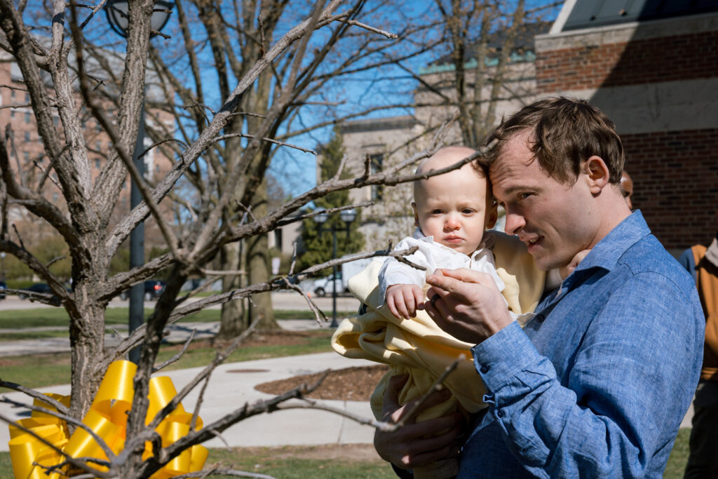 A man holding his young son and touching a small tree
