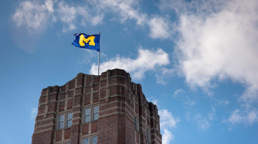 The flag on top of the Michigan Union flaps against a partly cloudy blue sky on a sunny day in mid-February. Image credit: VP Communications, Regents of the University of Michigan