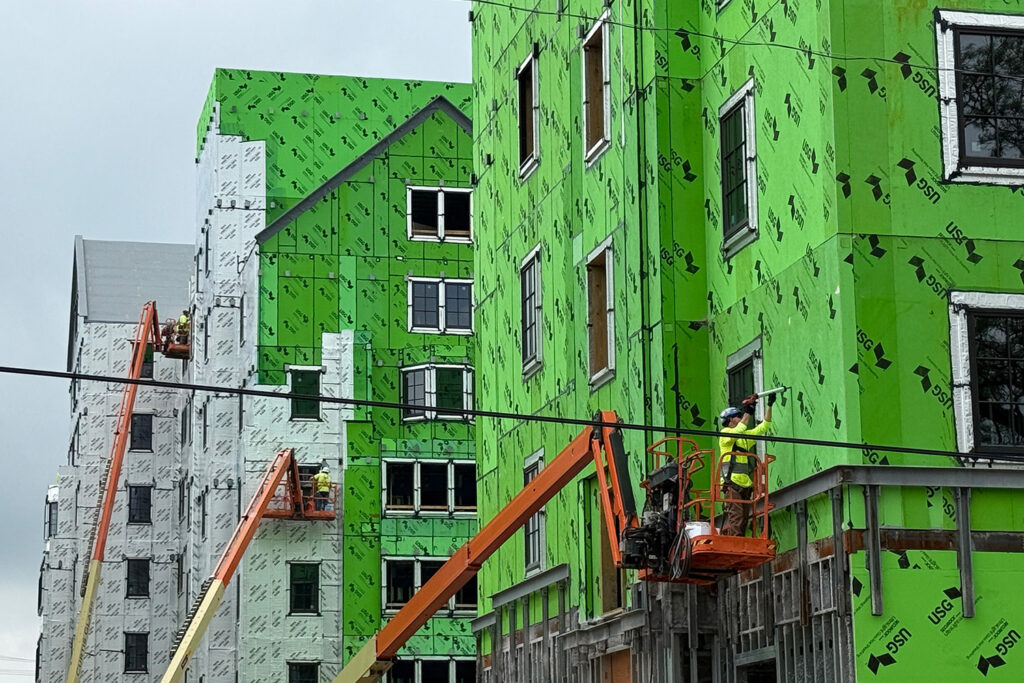 Three people in lifts working on buildings under construction