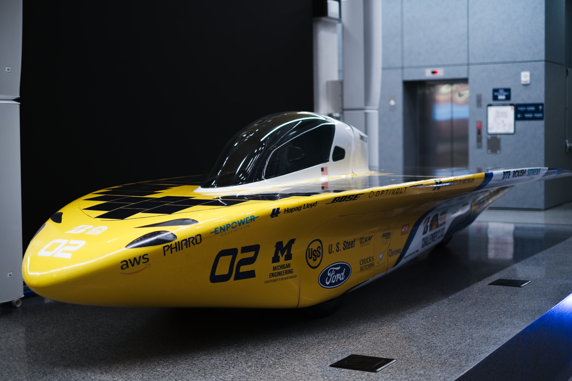 Millennium is parked in the atrium of a building with a gray, linoleum floor. Its sleek yellow body gleams as it reflects the atrium's fluorescent lights.