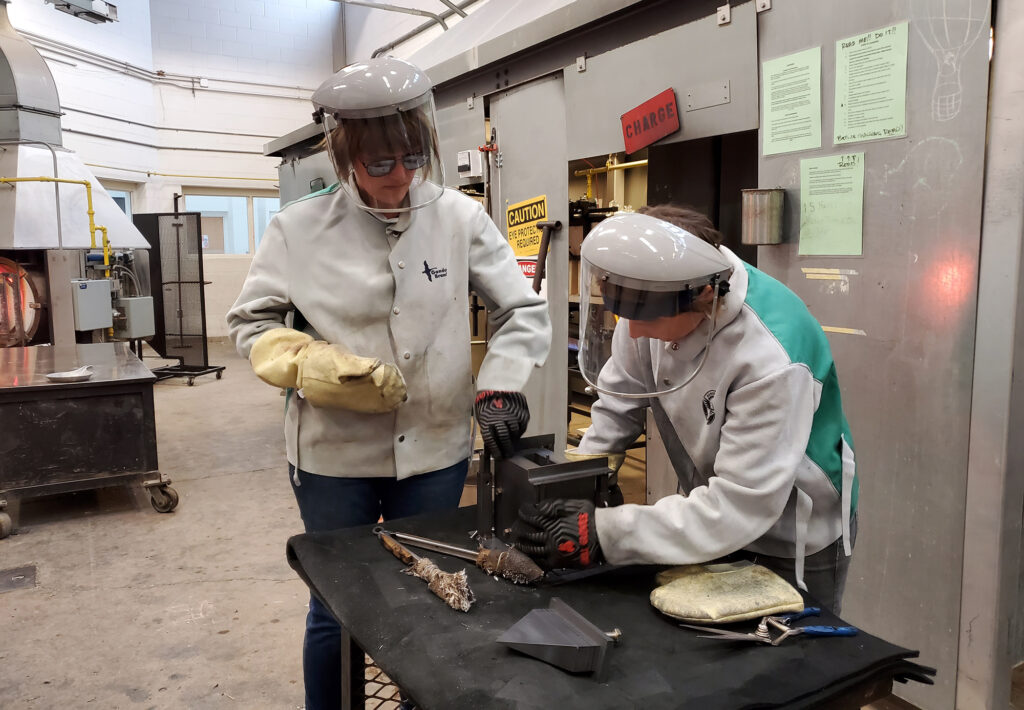 Two people wearing protective clothing while working with hot glass