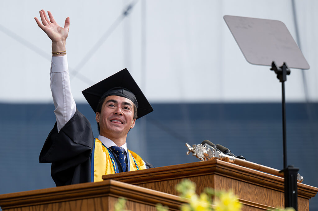 Lucas Solomon waves from the podium at the Spring Commencement.
