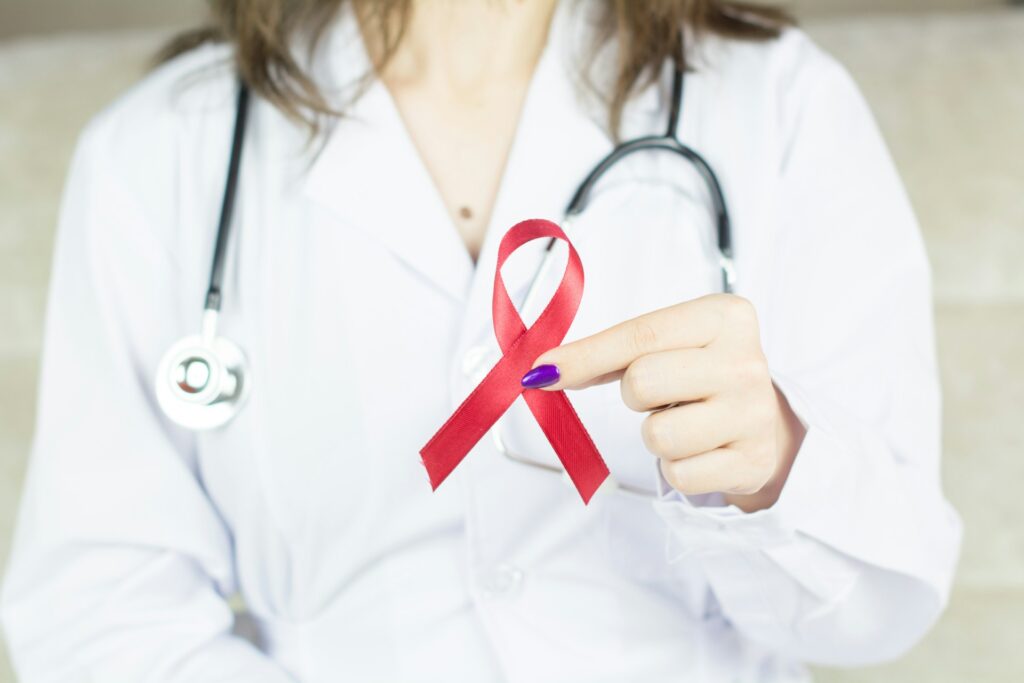 Doctor holding red ribbon HIV, world AIDS day awareness ribbon. Image credit: Bermix Studio, Unsplash.com