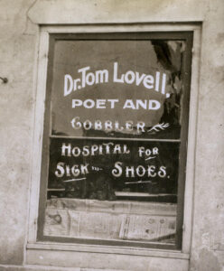 A storefront sign for a shoe repair shop on Huron Street in Ann Arbor, circa 1920, stating "Dr. Tom Lovell, poet and cobbler, hospital for sick shoes."