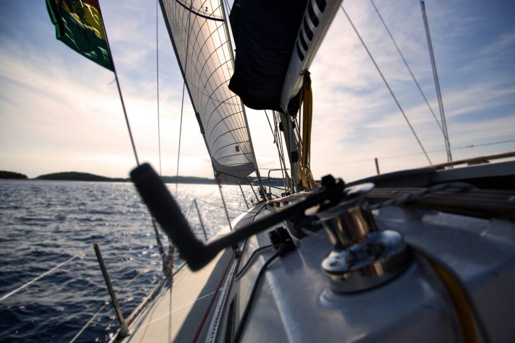 A view of blue water and a distant shoreline from the bow of a sailboat.