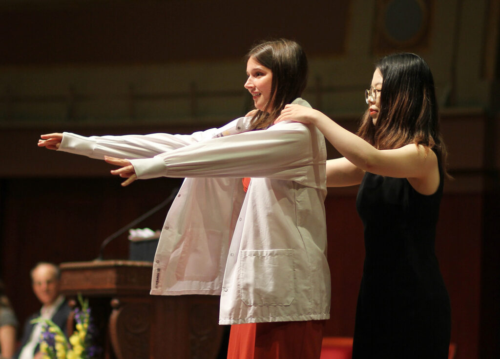A woman receives her white coat at a ceremony