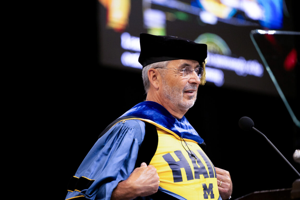 A man pulls back a robe to reveal a shirt with the word "HAIL" on it