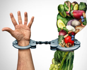 A handcuff restricts a hand created from healthy fruits and vegetables.