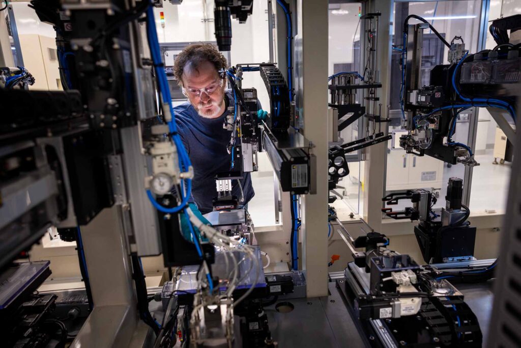 A man wearing safety glasses works amidst intricate machinery in a laboratory setting.