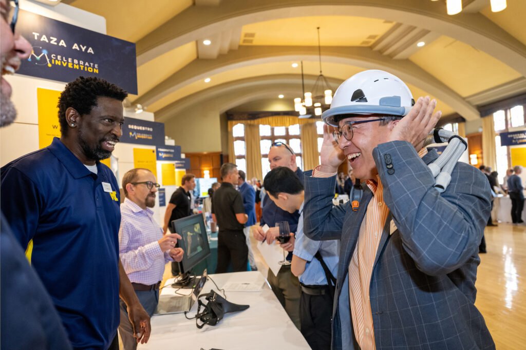 Taza Aya co-founder Herek Clack, left, watches as James Kim tries on an protective helmet which provides maskless personnel protection against airborne viruses during Celebrate Invention.