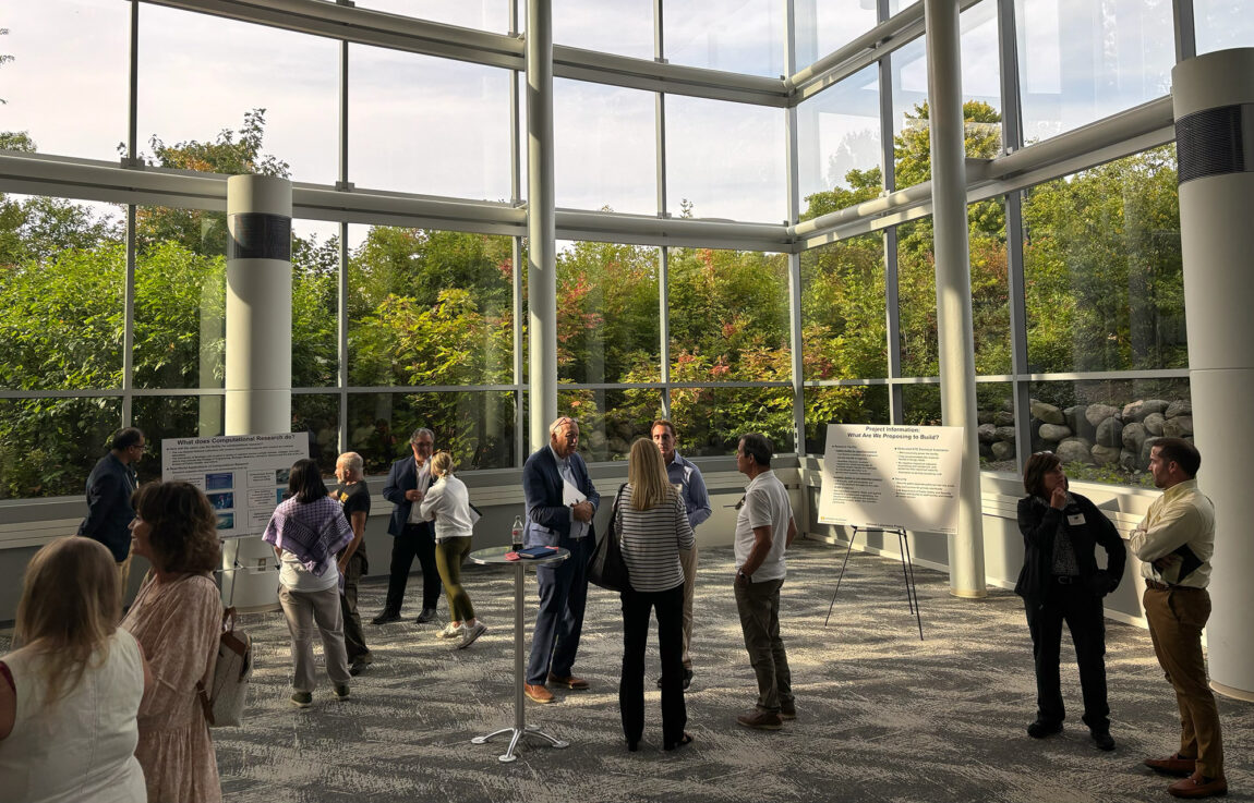 People inside a sunlit atrium of a building, standing around and talking while also looking at posterboards
