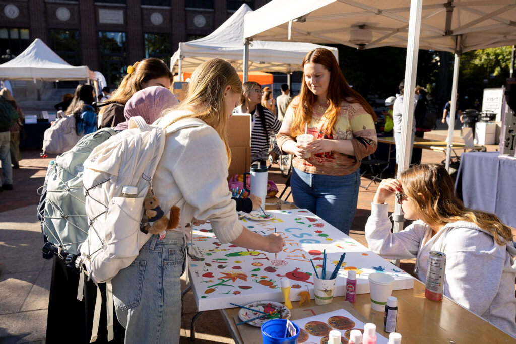 People stand around a table holding a large banner that can be painted