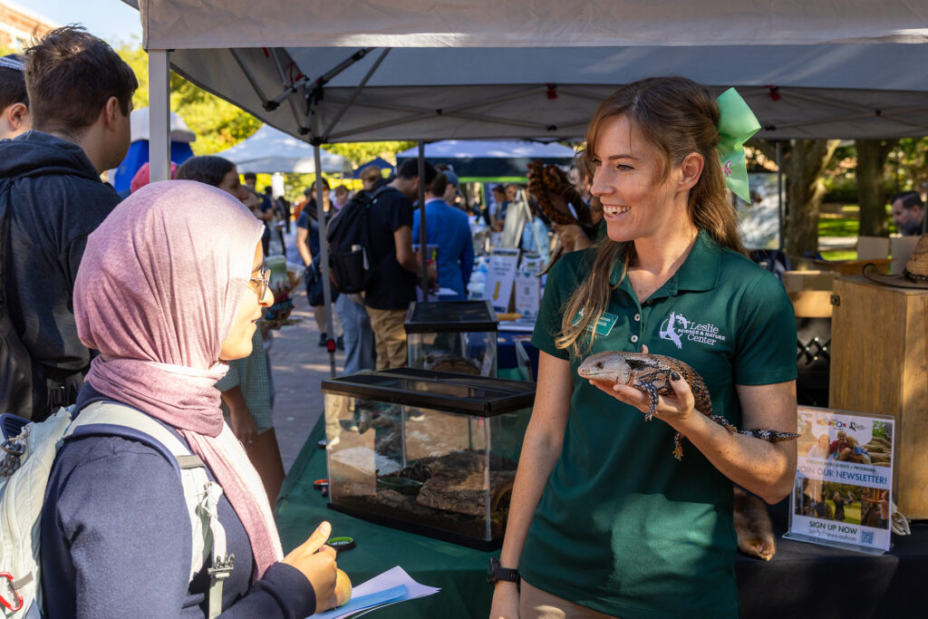 A woman holding an iguana smiles at another woman who has come to visit