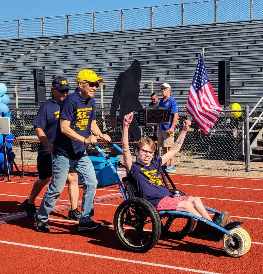 A man pushes a person in a wheeled vehicle on a running track
