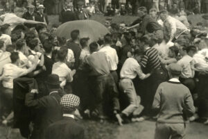 Black & white image dated 1911 shows rowdy University of Michigan men attempting to push a giant ball across a line while the opposing team defends their territory.