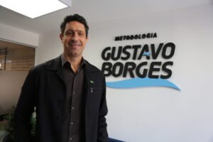 U-M graduate Gustavo Borges stands in front of an eponymous sign at his company in Sao Paulo, Brazil. His name is in black type with a light blue wave.