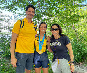 Gustavo Borges and wife stand amid green trees with U-M rowing superstar, daughter Gabriela.