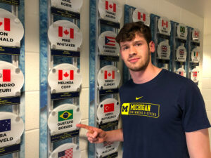 Luiz Gustavo Borges, dressed in a shirt for University of Michigan swimming and diving, points to his father's Olympic swim cap displayed at Canham Natatorium.