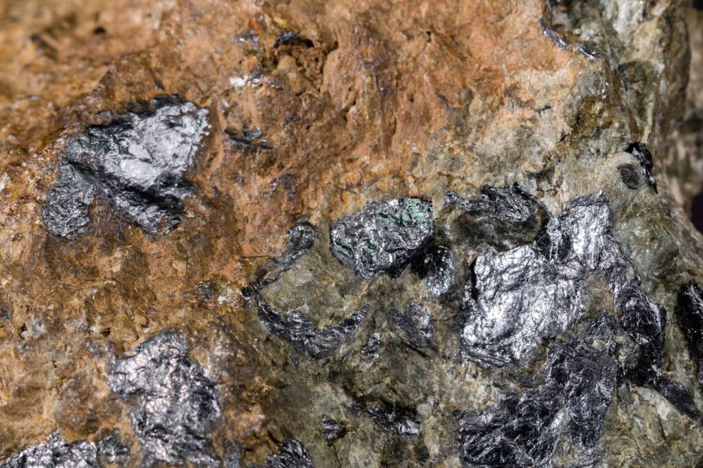 Lustrous black graphite crystals poke through an otherwise earth-toned rock.