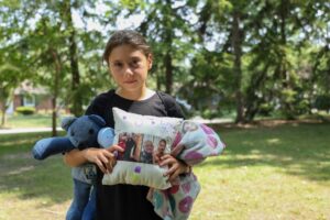 Estee Emery, 9, of Caro, lost her grandfather recently. She holds a pillow with her grandfather's photo that she decorated at camp. Hugging the pillows make the campers feel close with their loved ones. Image credit: Jeremy Marble, University of Michigan News