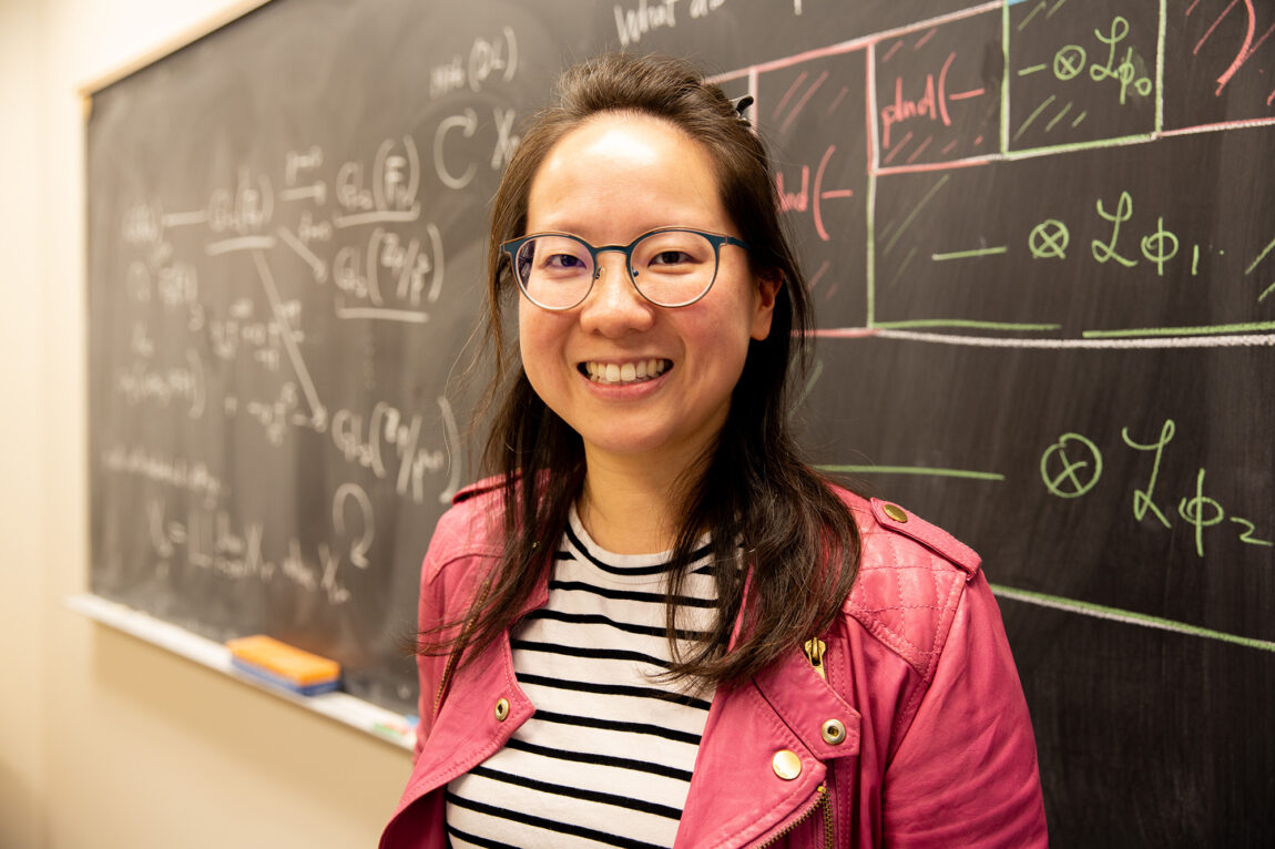 A woman standing in front of a chalkboard that displays math problems