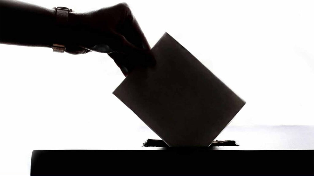 A hand places a ballot into a box. Image credit: Detroit Metro Area Communities Study