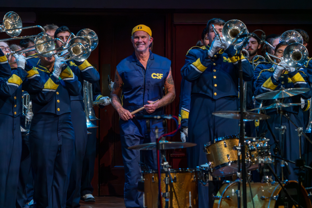 A drummer walks through a marching band on a stage to perform at a concert