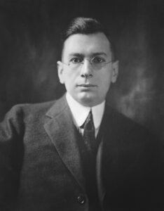 Black and white portrait of gentleman at the turn of the 20th century, wearing glasses and formal clothing.