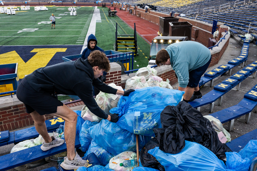 People in the grandstands of a stadium with bags of trash around them