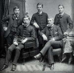 Black and white portrait of five well-appointed gentlemen in the late 29th century. William W. Cook is standing in the center.