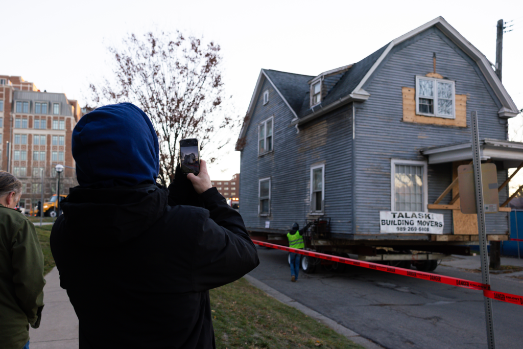 A person takes a photo or video with their phone while a house is moved down a street