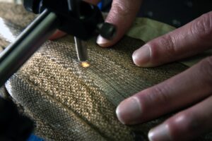 Close-up of hands measuring photonic fibers in light brown fabric. A small light point is focused on the fabric as the person's fingers gently press against the fabric as they conduct the analysis.