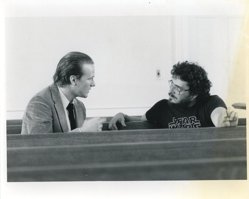 Two men sitting in a church pew looking at each other