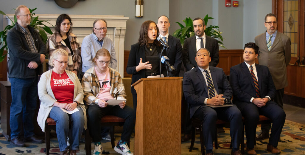 woman talking at podium with people sitting and standing behind her.